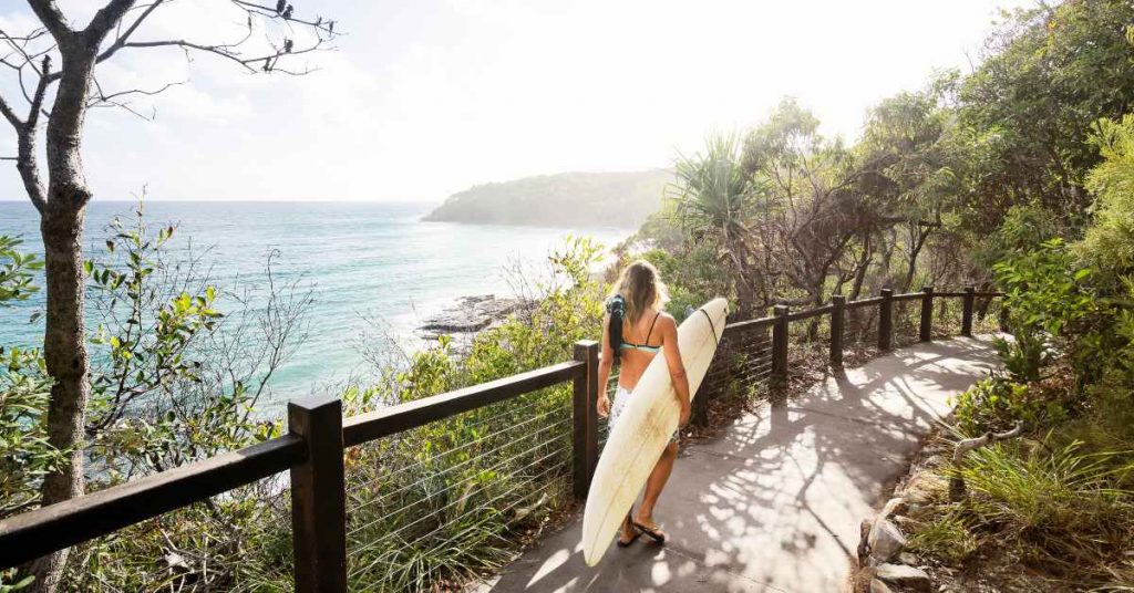 Woman with surfboard walking to the beach at Noosa