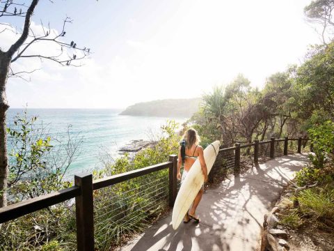 Woman with surfboard walking to the beach at Noosa